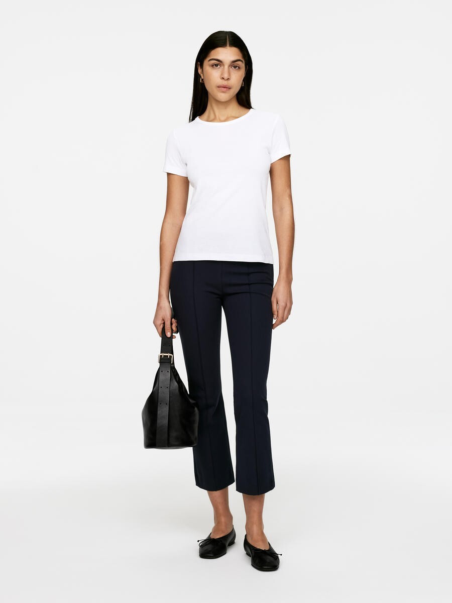 Woman in white shirt and dark trousers holding a black bag.